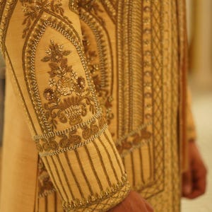 K&ouml;nnte beinhalten: Ein golden besticktes Kleidungsst&uuml;ck mit komplizierten floralen und geometrischen Mustern. Der Stoff hat einen dezenten Glanz und ist mit zarten Perlen verziert.