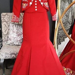 May include: A red dress with a matching jacket, both featuring gold and white embroidery. The dress has a fitted bodice and a flowing skirt with a mermaid silhouette.