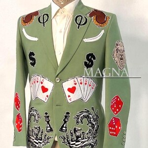 May include: A light green blazer with various embroidered designs, including playing cards, dice, chess pieces, and dollar signs. The blazer also features a lion's head and the word "MAGNATE".