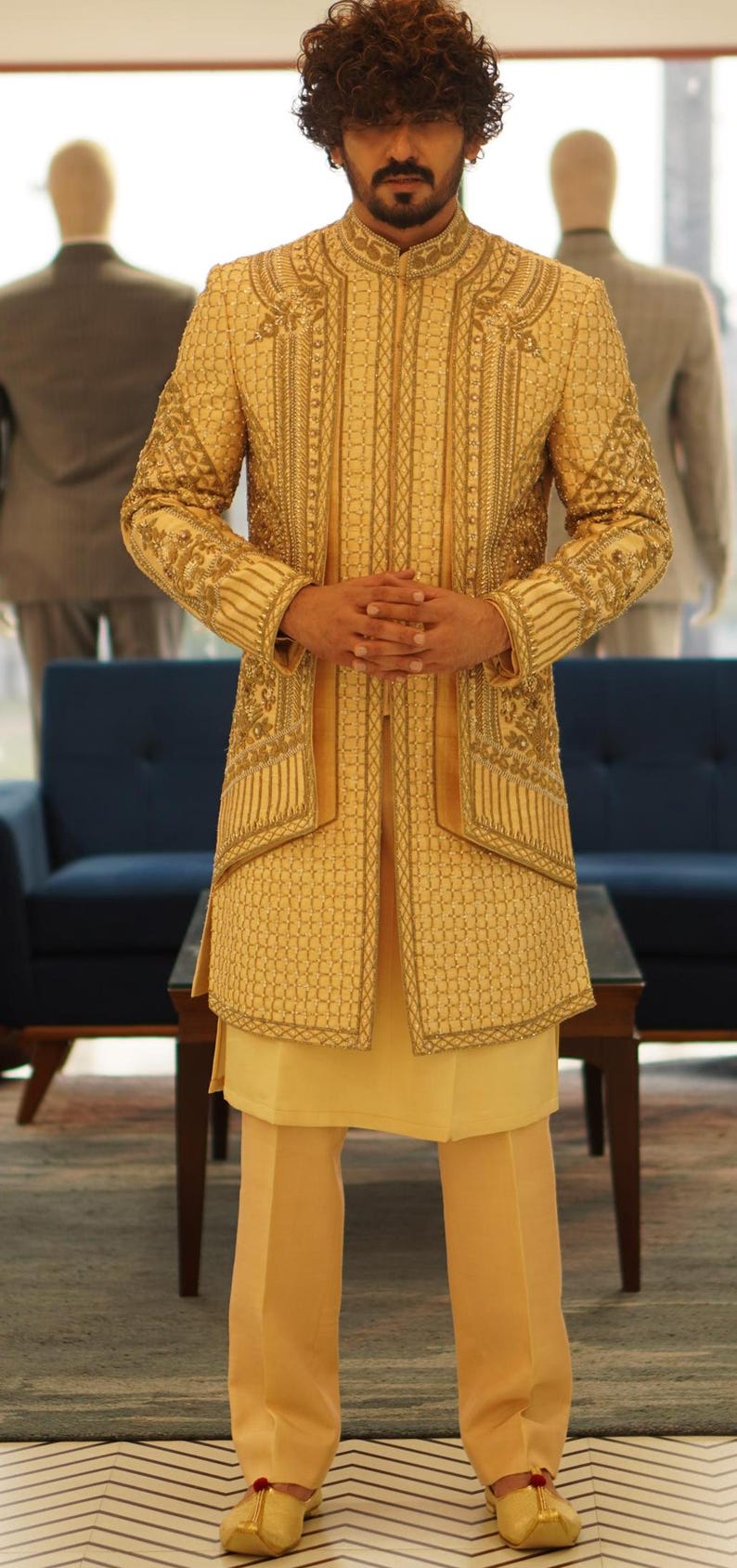 K&ouml;nnte beinhalten: Ein Mann tr&auml;gt eine goldene bestickte Jacke und eine passende Hose. Die Jacke hat einen Stehkragen und ein langes, flie&szlig;endes Design. Die Hose ist geschnitten und hat ein gerades Bein.
