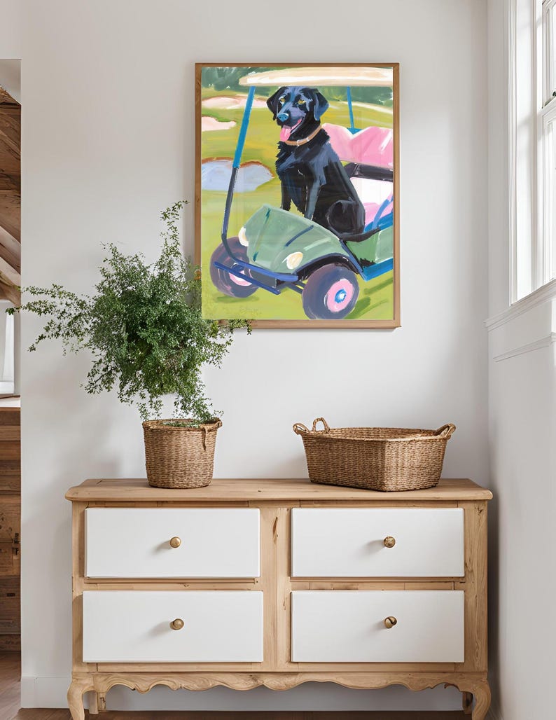 Puede incluir: Una pintura enmarcada de un perro negro sentado en un carrito de golf verde en un campo de golf. El perro lleva un collar rosa y tiene la lengua fuera.