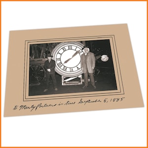Può includere: Una fotografia in bianco e nero di due persone in piedi davanti a un grande orologio. L'orologio è un accessorio del film Ritorno al futuro. L'iscrizione in basso dice "to Marty Partners in time September 5, 1885".