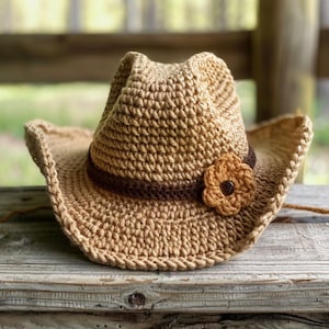 May include: A crocheted cowboy hat in tan and brown with a brown band and a crocheted flower accent.