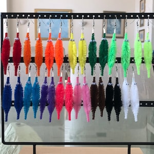 May include: A display of colorful pipe cleaner earrings with googly eyes. The earrings are arranged on a black stand with a wooden base.