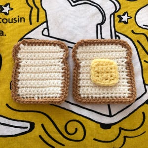 May include: Two crocheted coasters shaped like slices of toast. One coaster is plain, while the other has a square of yellow crochet, resembling butter. The coasters have a brown border and a cream-colored center, set against a yellow background.