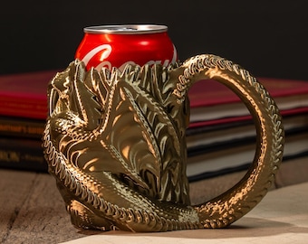 May include: A gold-colored dragon-themed can holder with an ornate handle, holding a red Coca-Cola can. The holder is detailed with scales and a dragon's head. The background includes books, candles, and a golden jar.