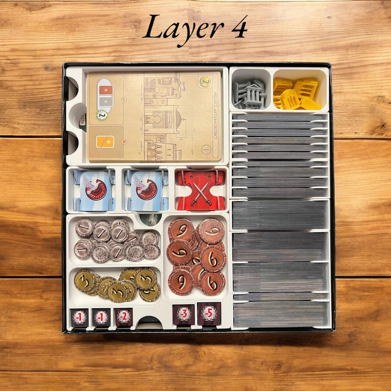 May include: Layer 4 of a board game organizer insert. The insert has compartments for cards, tokens, and other game components. The insert is made of white plastic and has a black border. The text "Layer 4" is printed on the top of the insert.