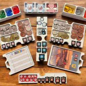 May include: A white plastic organizer with compartments for storing game pieces. The organizer has a variety of compartments, including some with dividers. The compartments contain a variety of game pieces, including coins, tokens, and cards. The organizer is designed to help players keep their game pieces organized and easy to access.