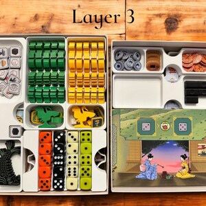 May include: A white plastic organizer with multiple compartments for storing game pieces. The organizer is labeled "Layer 3". The compartments contain various colored plastic pieces, dice, and a small illustration of a fish.