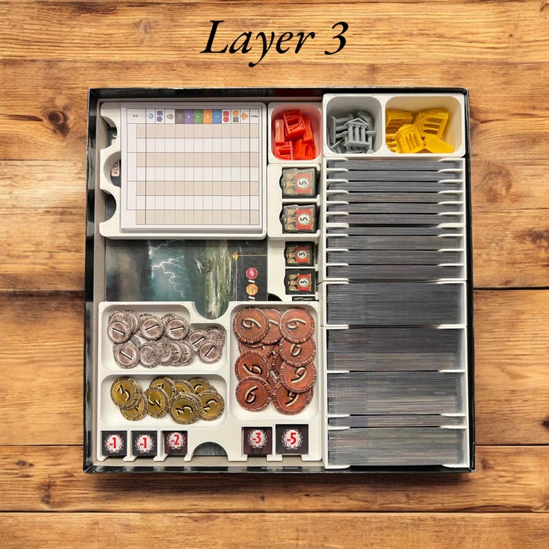 May include: Layer 3 of a board game organizer with compartments for cards, tokens, and dice. The organizer is white with black trim and has a label that says "Layer 3".