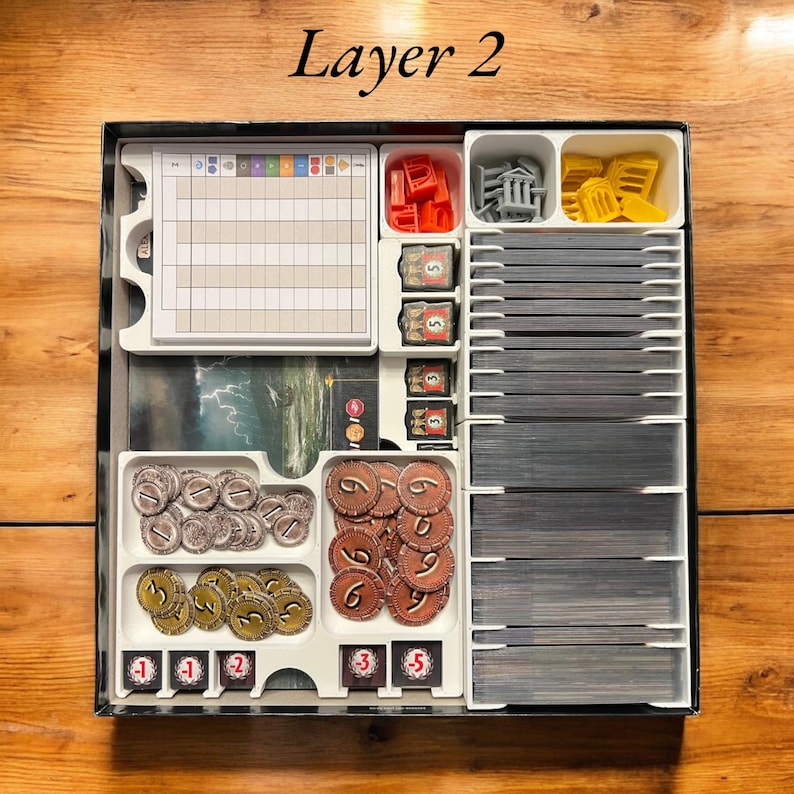 May include: A white plastic organizer with compartments for storing game pieces. The organizer has a label that says "Layer 2". The compartments contain small plastic tokens, dice, and cards.
