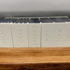 May include: A set of white boxes with the words "Armada", "Cities", "Leaders", "Age I", "Age II", "Guilds", and "Age III" printed on them.