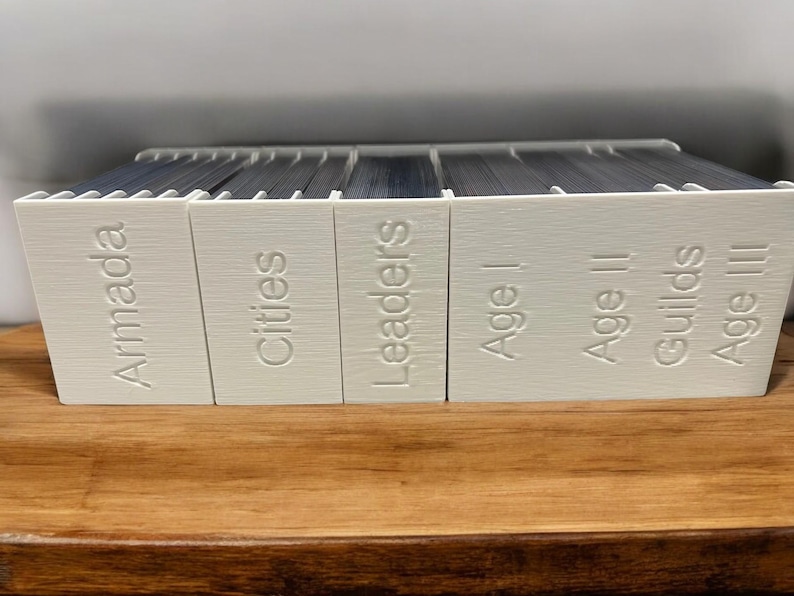 May include: A set of white boxes with the words "Armada", "Cities", "Leaders", "Age I", "Age II", "Guilds", and "Age III" printed on them.