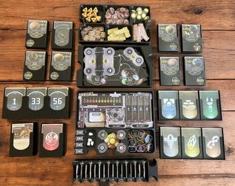 Könnte beinhalten: Ein schwarzer und grauer Spielorganizer mit Fächern für Karten, Spielsteine und Würfel. Der Organizer hat einen transparenten Kunststoffeinsatz mit einer Karte und einem Raumschiffdesign. Der Organizer ist mit den Zahlen 1, 33 und 56 beschriftet.