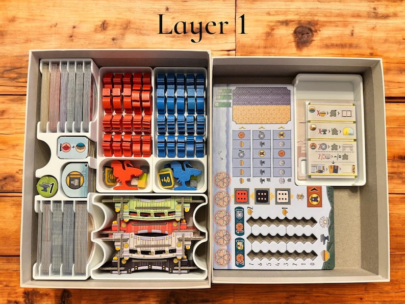 May include: A white plastic organizer with multiple compartments for storing game pieces. The organizer is labeled "Layer 1". The compartments contain various colored plastic pieces, dice, and cards.