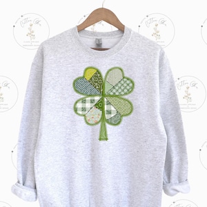 May include: A gray sweatshirt with a green four-leaf clover design made of different patterned fabric squares.