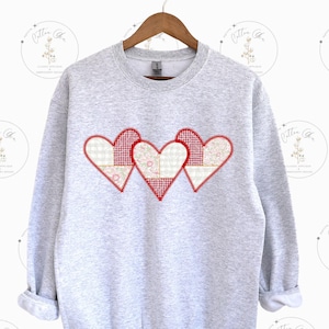 May include: A gray sweatshirt with three red patchwork hearts on the front. The hearts are made of white and pink fabric with a red gingham pattern.