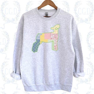 May include: A light gray sweatshirt featuring a patchwork lamb design. The lamb is composed of various fabric patterns, including floral, gingham, and geometric prints in pastel colors. The sweatshirt has a crew neck and long sleeves.