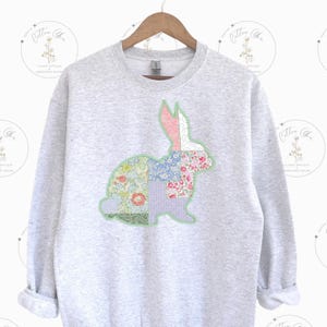 May include: A grey sweatshirt featuring a patchwork bunny design in shades of pink, blue, green and white. The bunny is outlined in green.