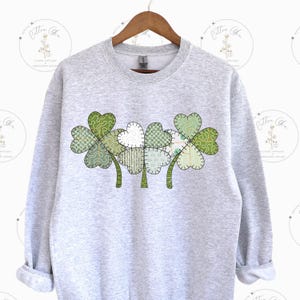 May include: A gray sweatshirt with a green, patchwork shamrock design. The shamrock is made up of multiple green and white fabric pieces.