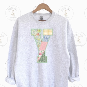 May include: A gray sweatshirt with a large patchwork letter Y on the front. The letter is made of different floral fabrics in shades of pink, blue, green, and yellow.