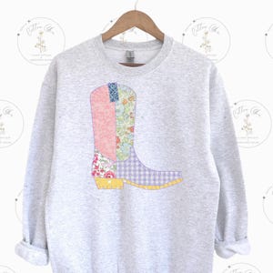 May include: A grey sweatshirt featuring a patchwork design of a cowboy boot in shades of pink, purple, yellow, and blue.