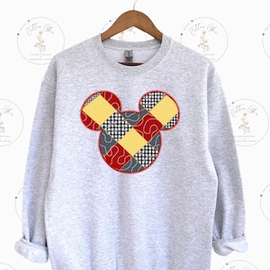 May include: A gray sweatshirt with a red, yellow, and black patchwork Mickey Mouse design.