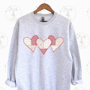 May include: A gray sweatshirt with three red, white, and pink patchwork hearts on the front.
