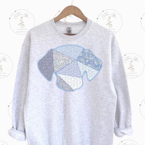 May include: A gray sweatshirt with a blue and white patchwork dog design on the front.