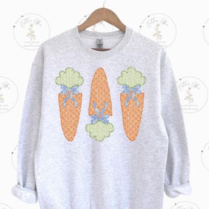 May include: A grey sweatshirt with three embroidered carrots on the front. The carrots are orange with green tops and blue bows.
