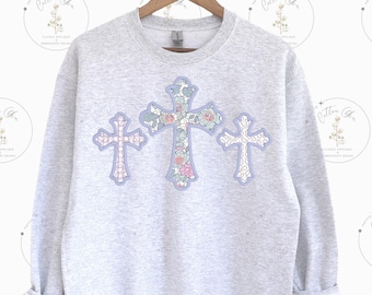 May include: A gray sweatshirt with three floral cross designs in shades of blue, pink, and green.