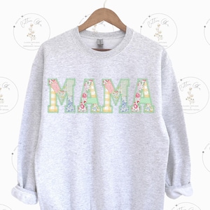 May include: A gray sweatshirt with the word "MAMA" spelled out in large, colorful letters. The letters are made of patchwork fabric with floral and checkered patterns.