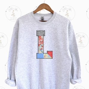May include: A gray sweatshirt with a large patchwork letter L on the front. The letter is made of different fabrics with floral and geometric patterns in shades of red, blue, and white.