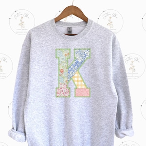 May include: A gray sweatshirt with a large patchwork letter K on the front. The letter is made of different floral fabrics and is outlined in green.