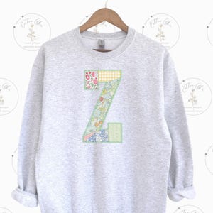 May include: A gray sweatshirt with a large patchwork letter Z on the front. The letter is made of different floral and patterned fabrics in shades of pink, green, yellow, and blue.