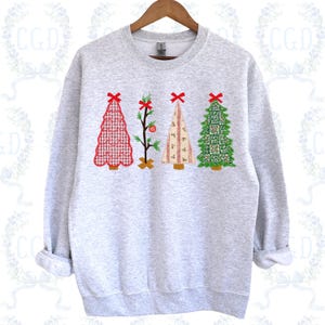 Könnte beinhalten: Ein hellgraues Sweatshirt mit vier Weihnachtsbaum-Designs. Die Bäume sind in verschiedenen Stilen gehalten, darunter ein rotes Vichy-Muster, ein spärlicher Baum mit einer Verzierung, ein gestreifter Baum und ein grüner Baum mit quadratischem Muster, jeder mit einer roten Schleife.