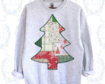 May include: A light gray sweatshirt with a Christmas tree design. The tree is made of green, red, and white patchwork fabric. The tree is stitched onto the sweatshirt with a zig-zag stitch. The sweatshirt is hanging on a wooden hanger.
