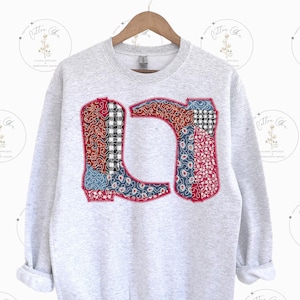 Może przedstawiać: Szara bluza z patchworkowym wzorem dwóch kowbojskich butów. Buty są wykonane z różnych materiałów i kolorów, w tym czerwonego, niebieskiego i białego.