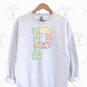 May include: A gray sweatshirt with a large patchwork letter "P" on the front. The letter is made of different floral fabrics in shades of pink, yellow, green, and blue.