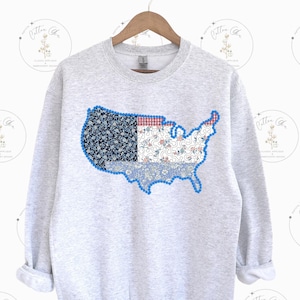 May include: A gray sweatshirt with a patchwork design of the United States of America. The patchwork is made up of various floral patterns in shades of blue, red, and white.