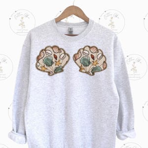 May include: A gray sweatshirt with a design of two seashells with various sea life inside. The shells are brown, white, and green.