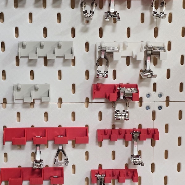 May include: A collection of sewing machine presser feet and holders, displayed on a white pegboard. The holders are in red, white, and gray, with the presser feet in silver. The pegboard has evenly spaced holes.