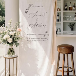 May include: A tall, off-white fabric banner hanging from a gold rod with a beige ribbon tie. The banner features black text reading: WELCOME TO Samuel & Adeline's ENGAGEMENT PARTY! 10. 08. 2025 | LONDON, ENGLAND We're so glad you're here! with illustrations.