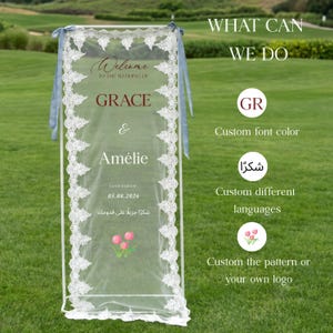 May include: A white wedding sign with lace trim and blue ribbons. The sign reads "Welcome to the wedding of Grace & Am&eacute;lie" with the date 05.08.2026. Additional text includes "What can we do" and options for customization.