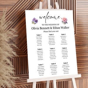 May include: A white wedding seating chart on an easel. The sign features the words "welcome" and "To the Wedding of Olivia Bennett & Ethan Walker." Floral accents and guest names are listed under table numbers.
