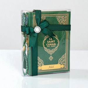 May include: A green book set, including a Quran, is presented in a clear box, tied with a dark green ribbon and a decorative white and silver embellishment. A matching green beaded prayer accessory is included. The book cover features gold filigree and the text "LE SAINT CORAN ARABE - FRAN&Ccedil;AIS".