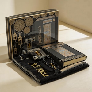 Op de afbeelding: Een zwarte geschenkdoos met gouden details, met een gebedskleed, een Koran, een parfumflesje en gebedskralen. De gebedskleed is zwart met gouden borduursel.
