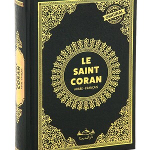 May include: A hardcover book with a black cover and gold decorative accents. The title "LE SAINT CORAN" is displayed in a gold circular frame. The book's spine reads "CORAN ARABE-FRAN&Ccedil;AIS".
