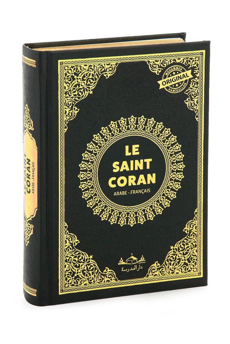 May include: A hardcover book with a black cover and gold decorative accents. The title "LE SAINT CORAN" is displayed in a gold circular frame. The book's spine reads "CORAN ARABE-FRAN&Ccedil;AIS".