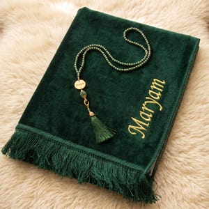 Op de afbeelding: Een donkergroen fluwelen gebedskleed met een franjerand en de naam Maryam geborduurd in gouddraad. Een bijpassende groene kralen gebedsketting met een gouden ronde hanger gegraveerd met de naam Maryam en een groene kwast.
